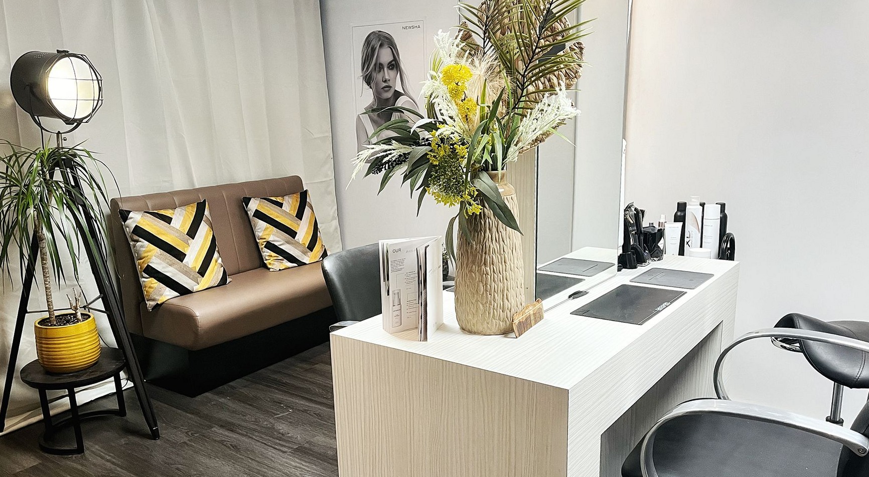 De salon: een leren bank met zwart-gele kussens, een spiegeltafel met bloemen en een kappersstoel